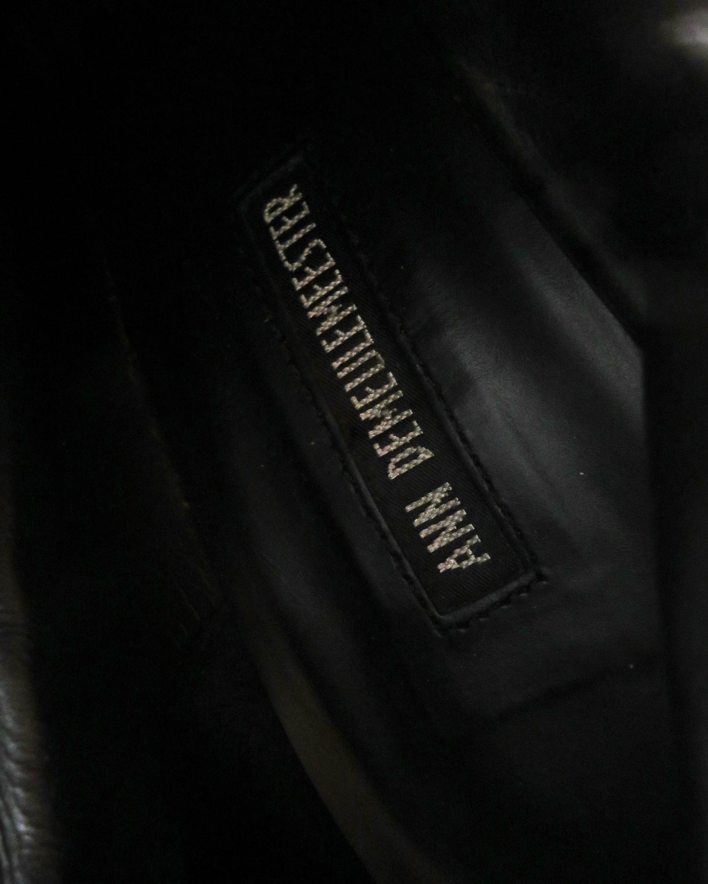 Close-up of a black leather jacket with a brand label on a dark background