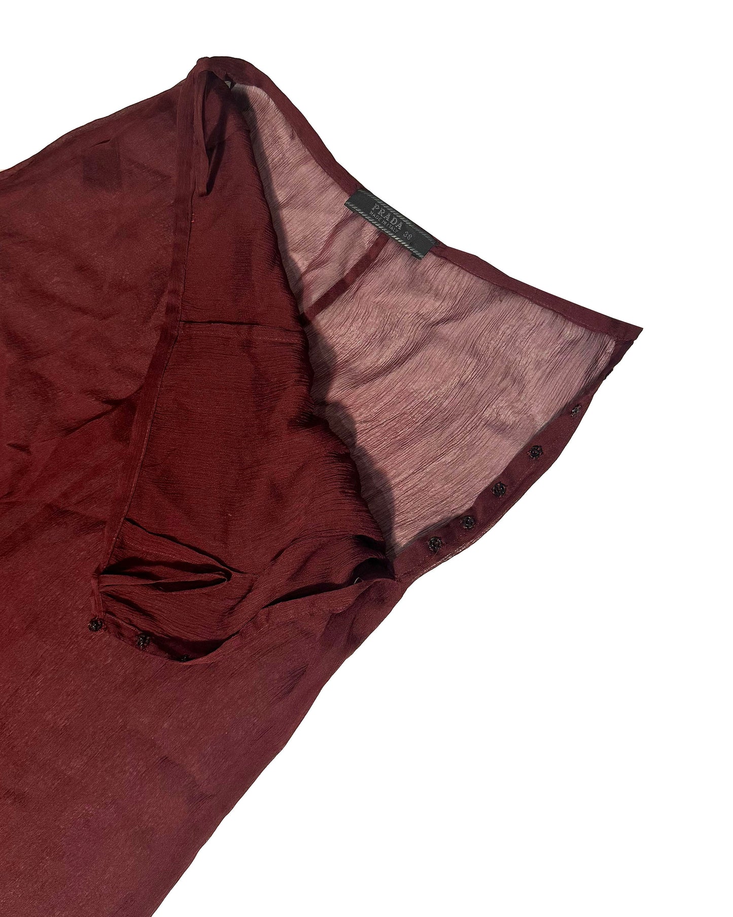 A close-up of a dark burgundy or maroon sheer mesh garment, showing the fabric texture and a small black brand label that reads 'SARAH', set against a plain white background.