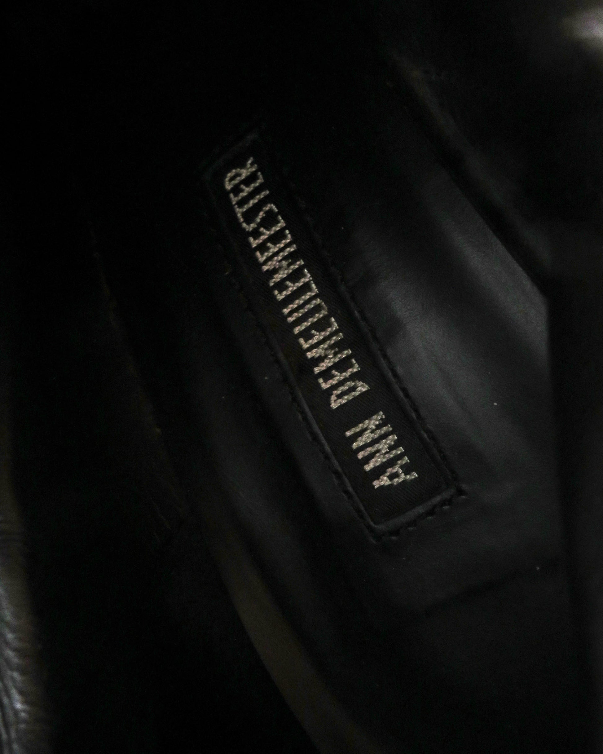 Close-up of a black leather jacket with a brand label on a dark background