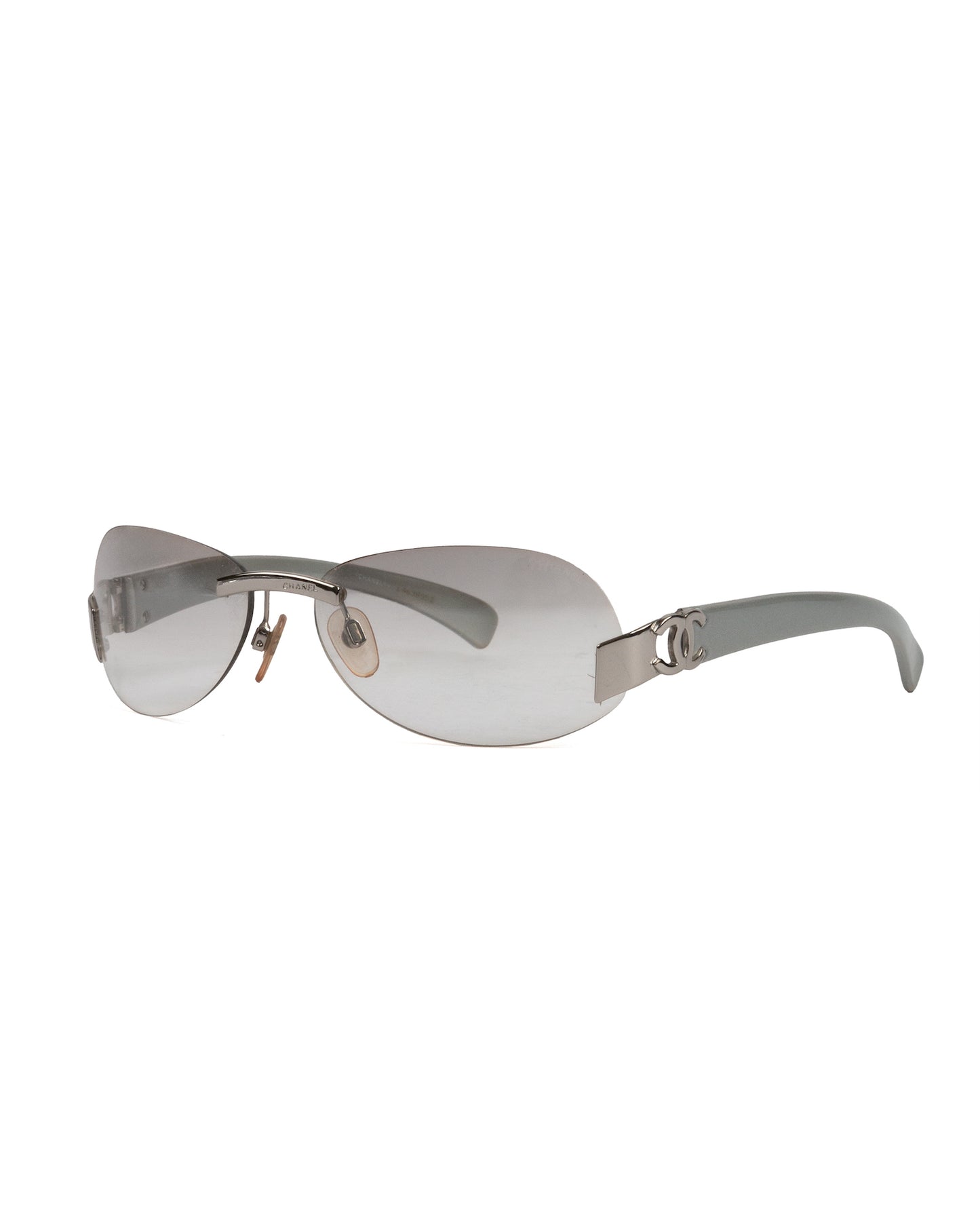 A pair of silver grey rimless oval sunglasses with the Chanel CC logo on the hinges.