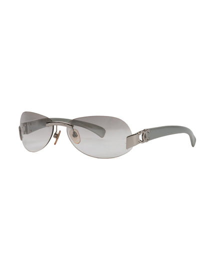 A pair of silver grey rimless oval sunglasses with the Chanel CC logo on the hinges.