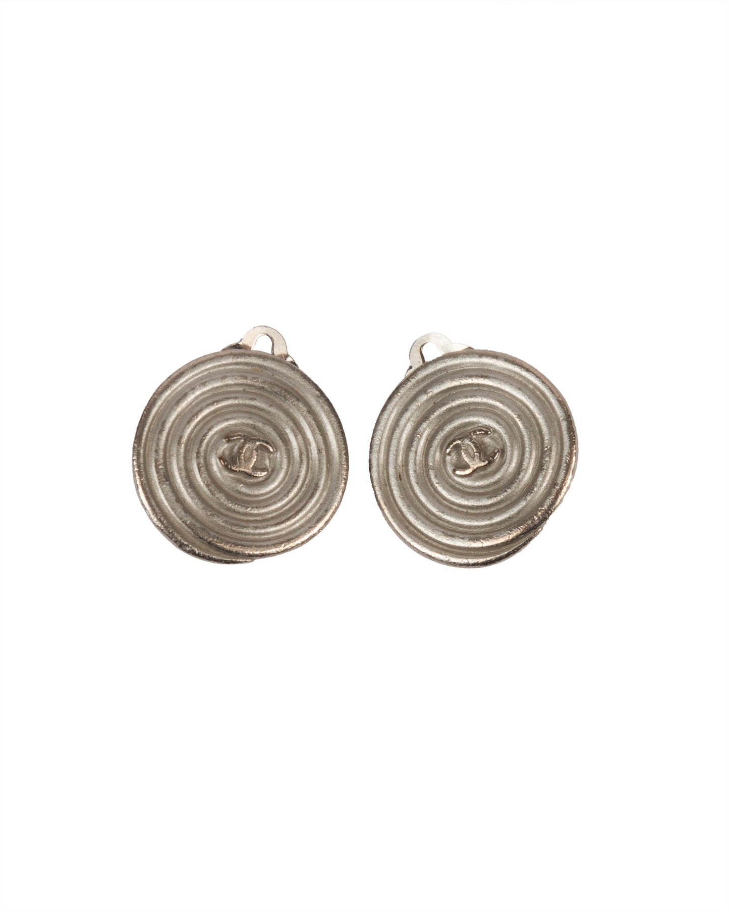 A pair of round silver-tone metal clip-on earrings with a spiral relief design and central CC logo.