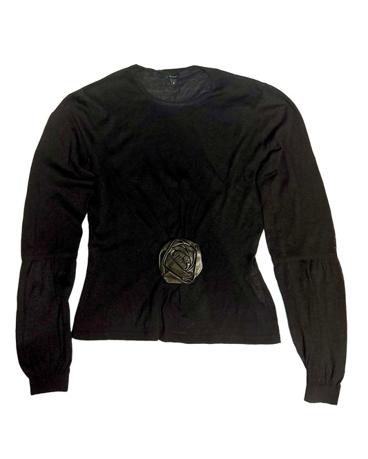 A black long-sleeve knit top with a gathered, ruched waist and a metallic rose-shaped embellishment at the center front, shown against a plain white background.