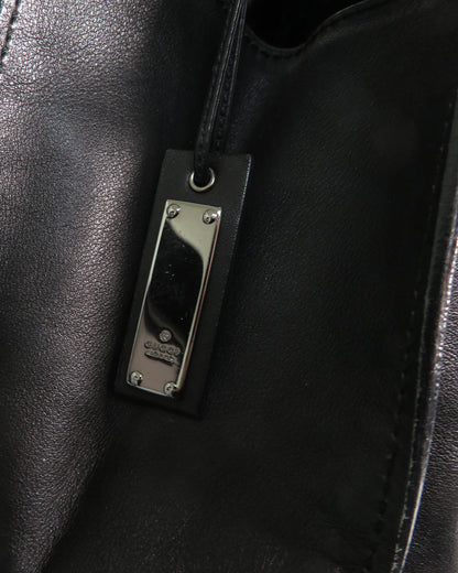 Close-up of a black leather bag with a metal tag featuring a brand logo.