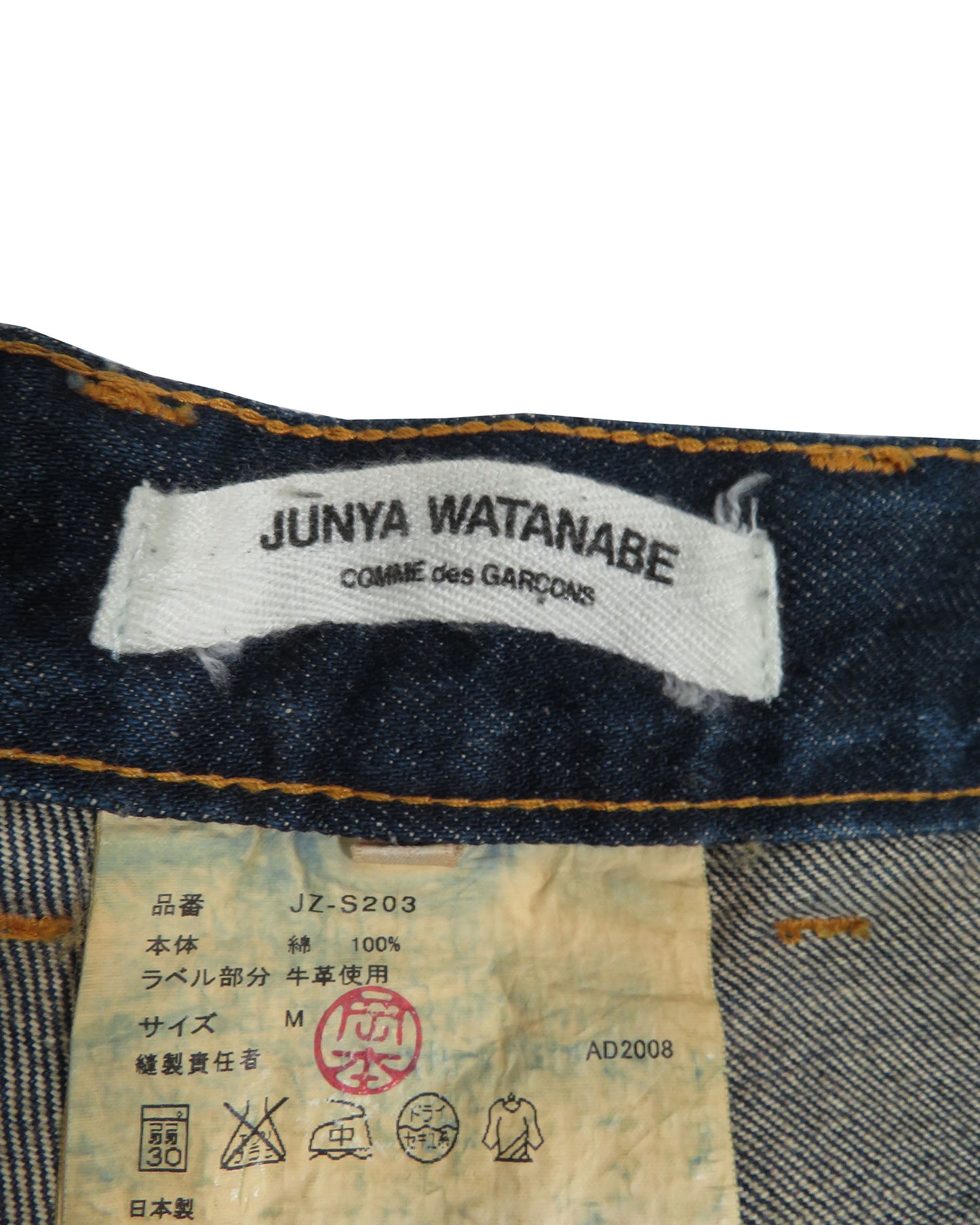 Close-up of Junya Watanabe label on denim fabric with additional labels below.