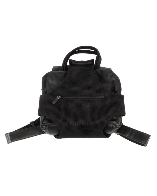 A black leather and mesh modular backpack with a detachable leather handle and a mesh harness, featuring a front zip pocket and an embossed Miu Miu logo.