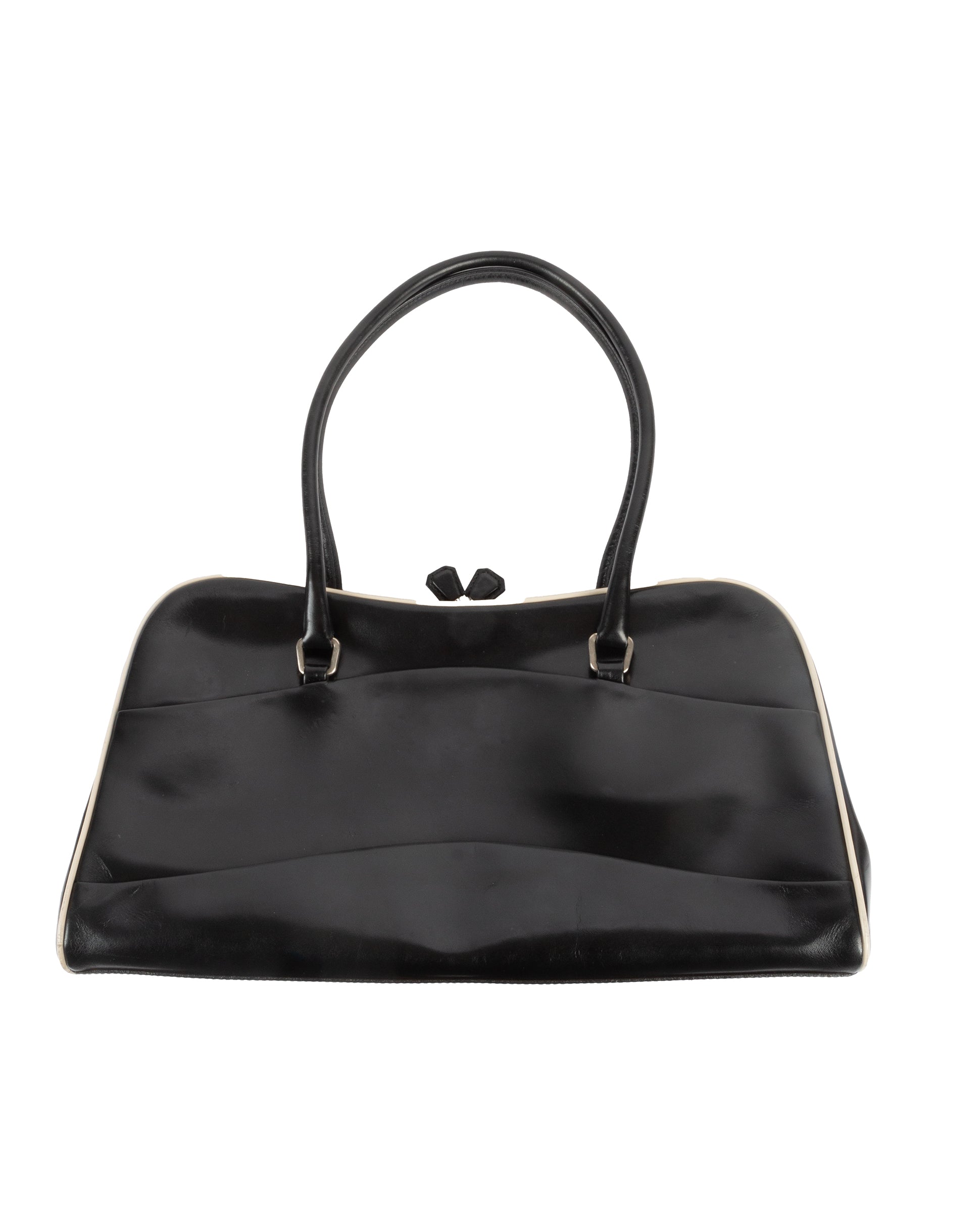 A black leather handbag with a kiss lock closure and double handles, featuring white piping along the edges and Prada's signature logo on the side.