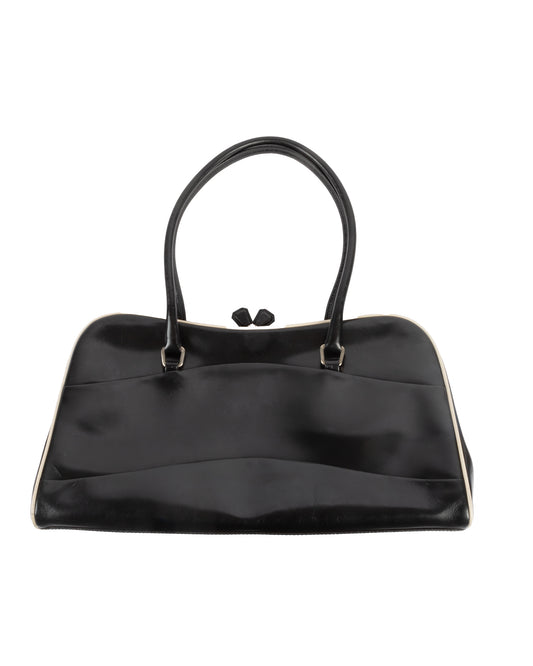 A black leather handbag with a kiss lock closure and double handles, featuring white piping along the edges and Prada's signature logo on the side.