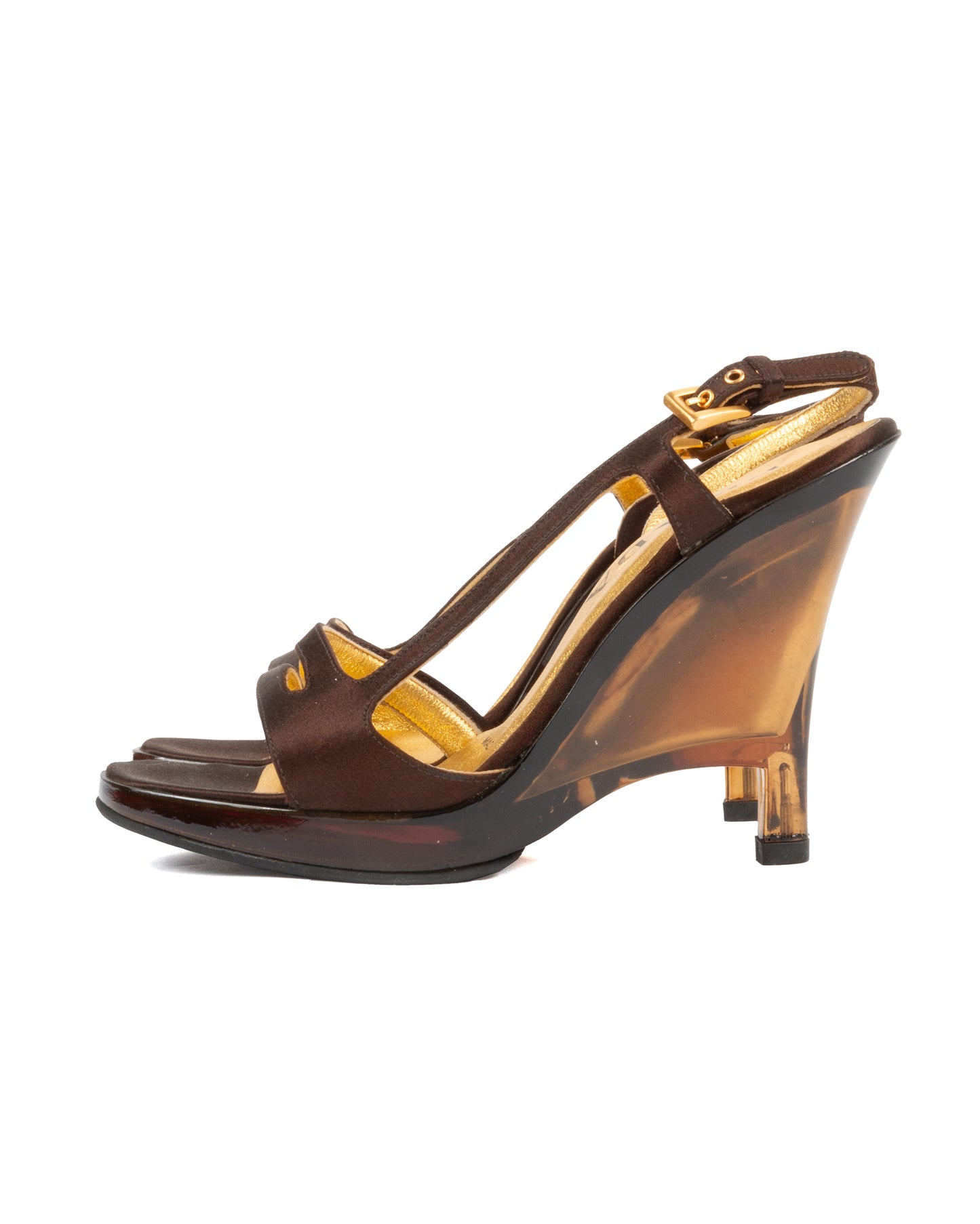A brown satin cut-out strap wedge sandal with a square toe and an amber-toned lucite wedge heel, featuring a gold metallic leather insole and slim front straps with an adjustable ankle strap and gold hardware.