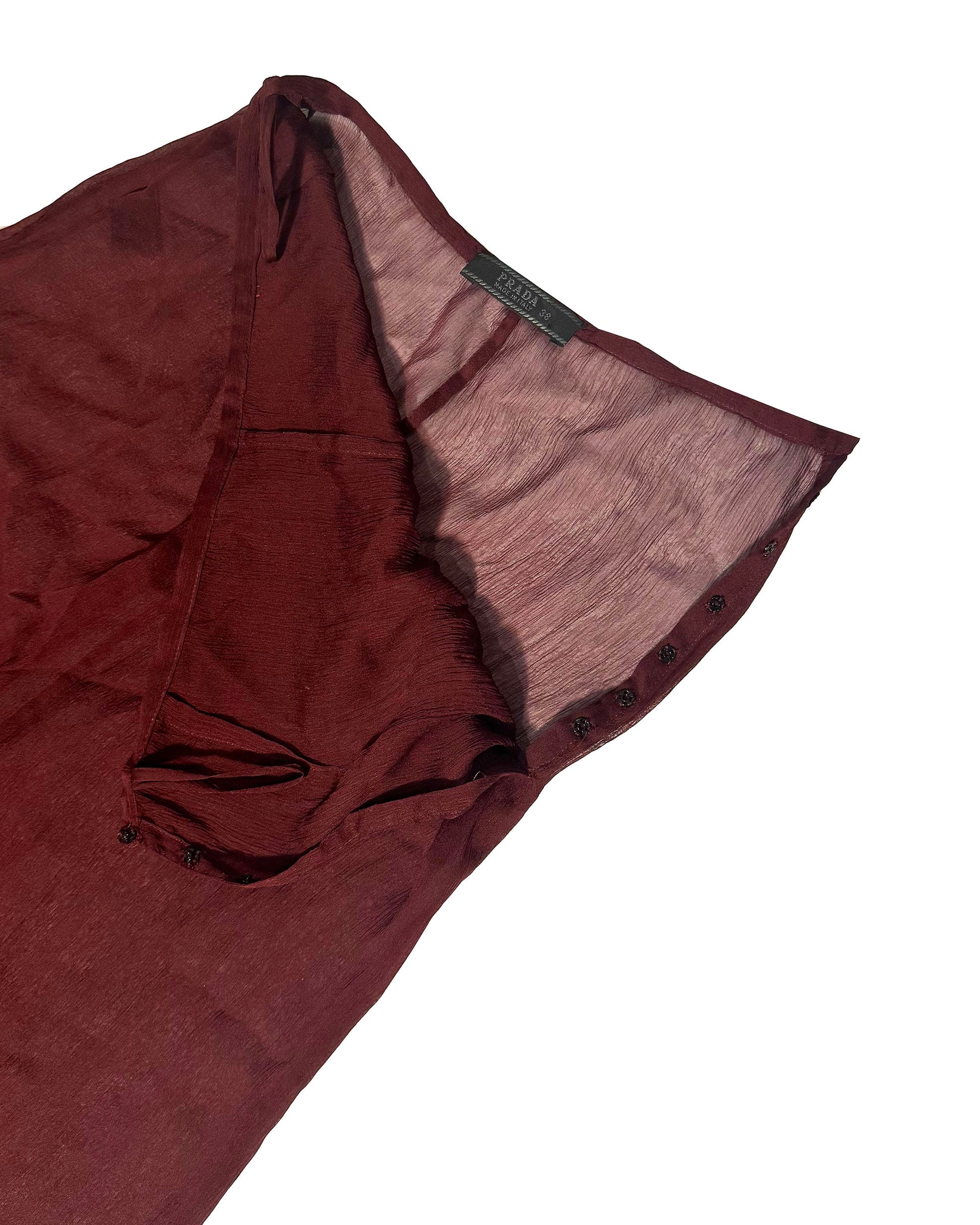 A close-up of a dark burgundy or maroon sheer mesh garment, showing the fabric texture and a small black brand label that reads 'SARAH', set against a plain white background.