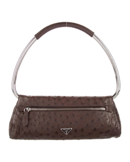A brown ostrich leather handbag from Prada with a structured silhouette, a distinctive curved metal handle, silver-tone hardware, an exterior zip pocket, and a triangular Prada logo plaque.