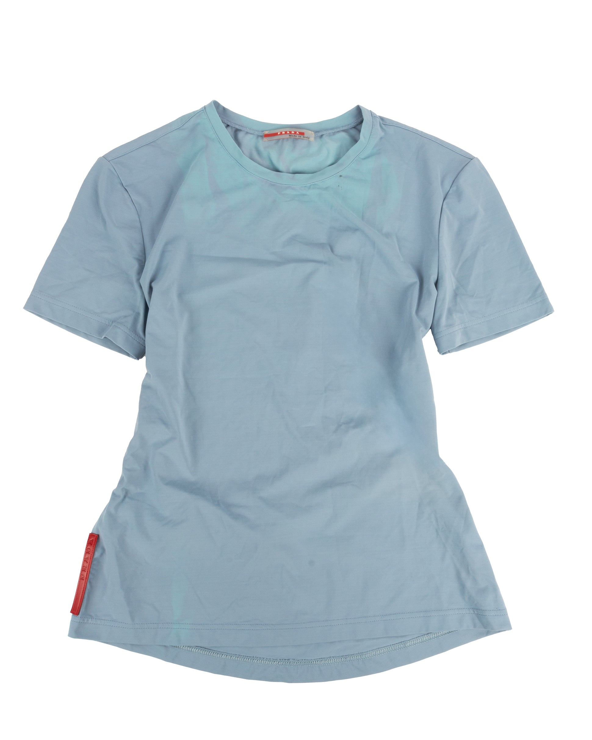 A powder blue short-sleeved technical t-shirt with a small zip pocket on the lower back and a red rubber Prada tag at the left hip.
