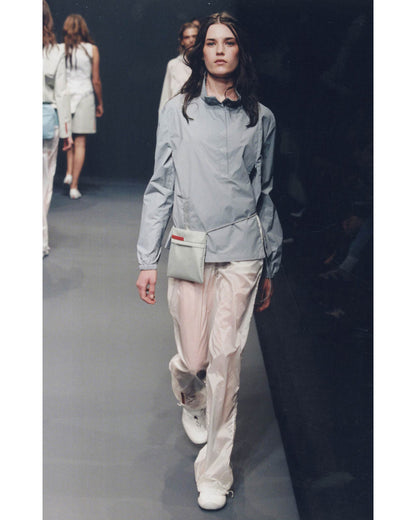 Model walking on a runway wearing a light gray jacket and beige pants.