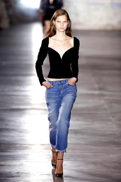 Model walking on a runway wearing a black top and blue jeans.