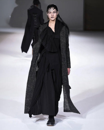 Model wearing a black outfit with a long coat on a runway.